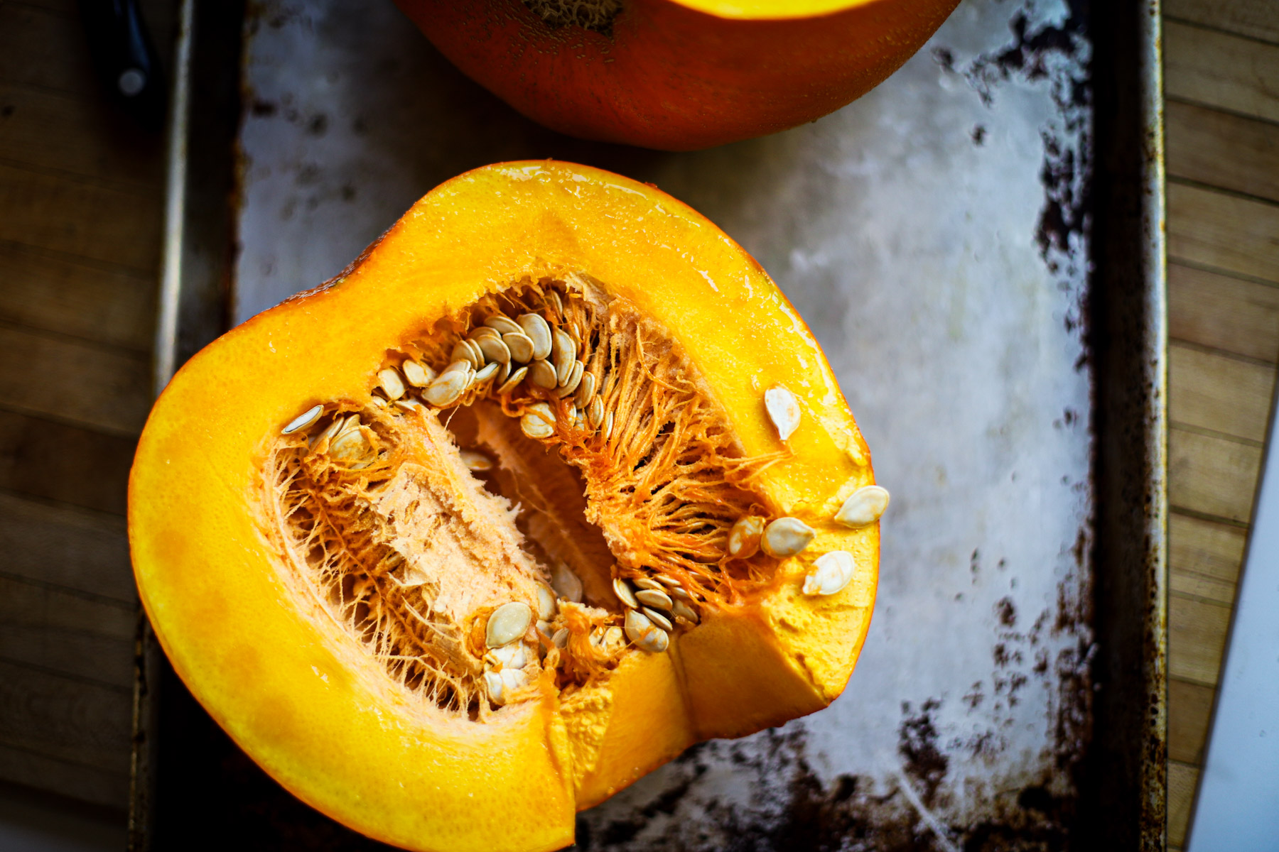 A halved pumpkin with visible seeds and fibrous interior rests on a metal baking tray, ready to be transformed into a hearty carrot pumpkin soup.