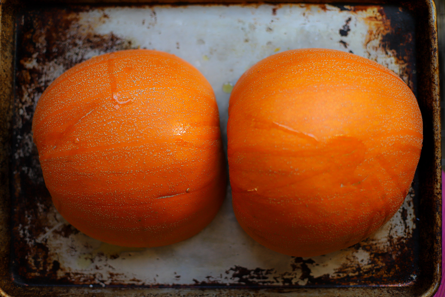 Top-down view of two roasted pumpkin halves, skin side up, on a frying pan.