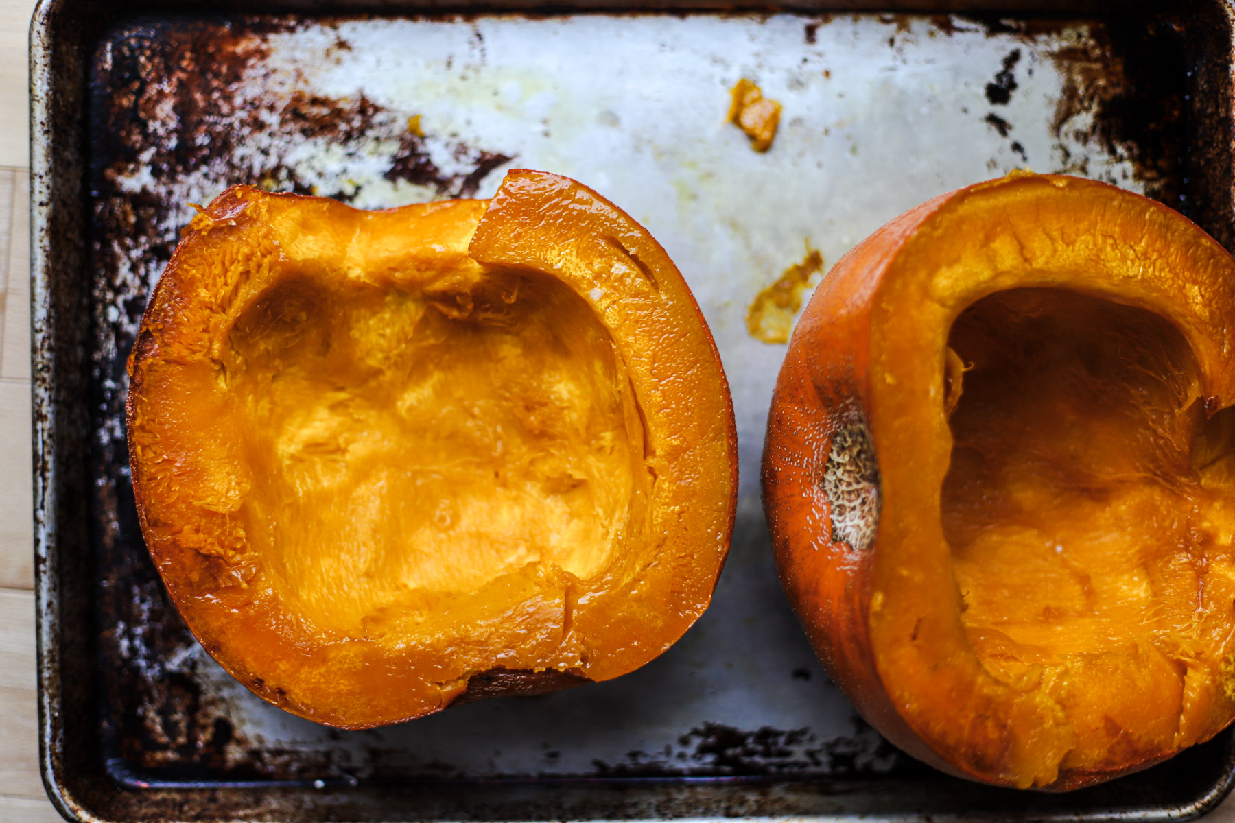 Top-down view of two roasted pumpkin halves on a frying pan after baking in the oven.