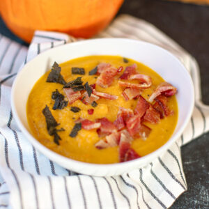 Closeup view of creamy carrot pumpkin soup topped with crispy bacon and fried sage.