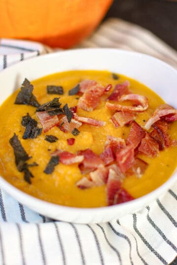 Closeup view of creamy carrot pumpkin soup topped with crispy bacon and fried sage.