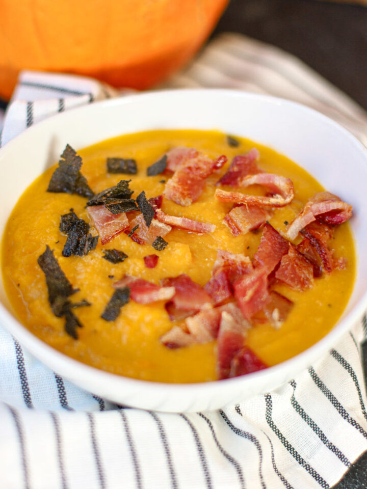 Closeup view of creamy carrot pumpkin soup topped with crispy bacon and fried sage.