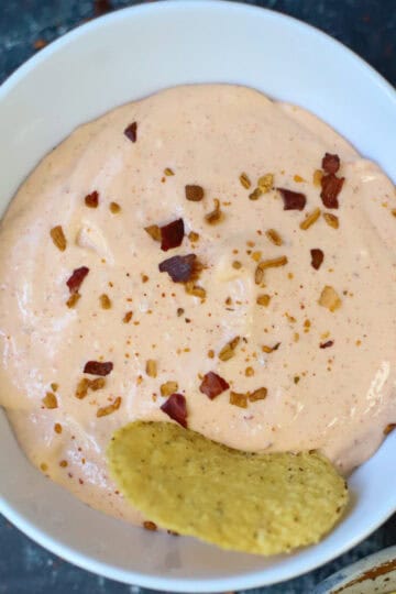 Close-up of creamy cottage cheese queso dip garnished with crushed red pepper flakes, served with a tortilla chip.