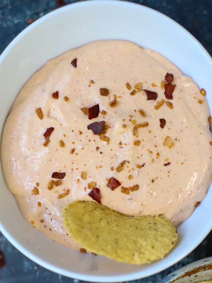 Close-up of creamy cottage cheese queso dip garnished with crushed red pepper flakes, served with a tortilla chip.