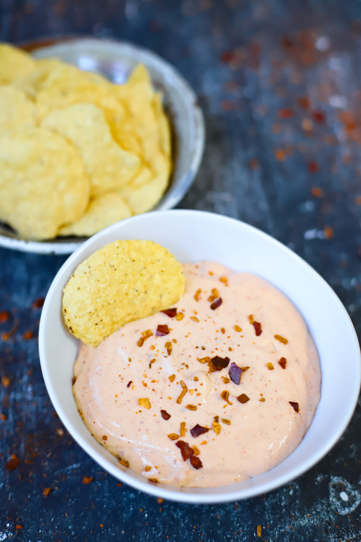 A bowl of creamy cottage cheese queso dip topped with crushed red pepper flakes, served with tortilla chips in the background