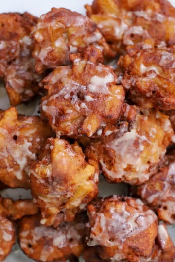 Close-up of golden-brown sourdough apple fritters drizzled with vanilla glaze, showcasing the crisp texture and apple chunks.