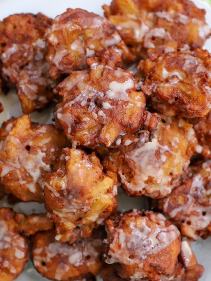 Close-up of golden-brown sourdough apple fritters drizzled with vanilla glaze, showcasing the crisp texture and apple chunks.