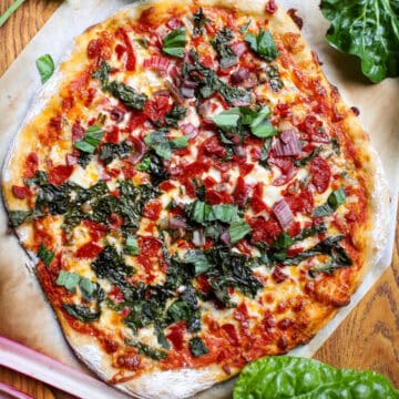 A Swiss chard and pepperoni pizza surrounded by Swiss chard and basil on a cutting board