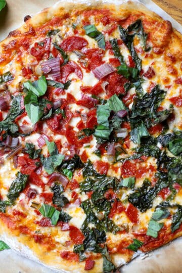 A top down view of a Swiss chard and pepperoni pizza on a cutting board