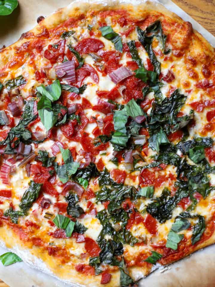 A top down view of a Swiss chard and pepperoni pizza on a cutting board