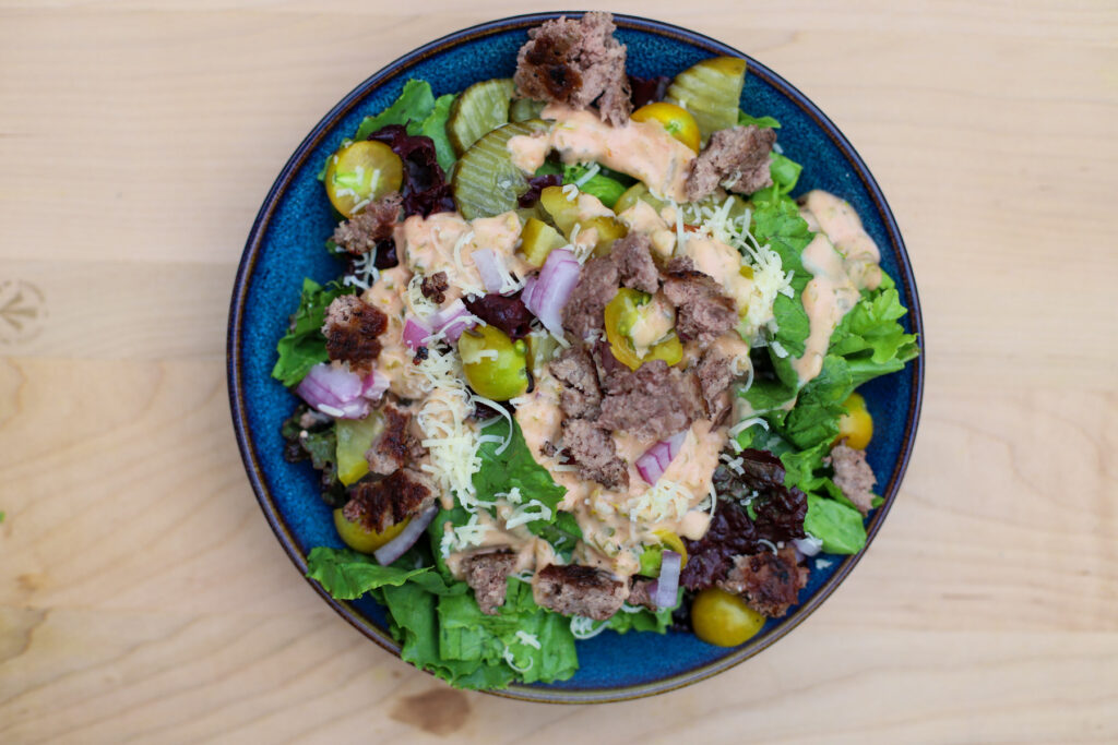 Top view of Big Mac salad in a blue bowl with lettuce, ground beef, pickles, shredded cheese, red onions, and special sauce on a wooden surface.