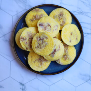 Close-up of fluffy cottage cheese egg bites with bacon on a dark blue plate over a marble countertop.