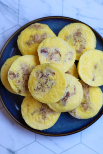 Close-up of cottage cheese egg bites with bits of bacon on a blue plate, set against a marble countertop.