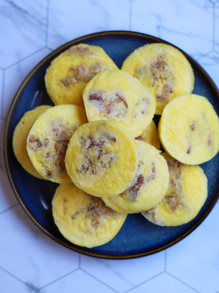 Close-up of cottage cheese egg bites with bits of bacon on a blue plate, set against a marble countertop.