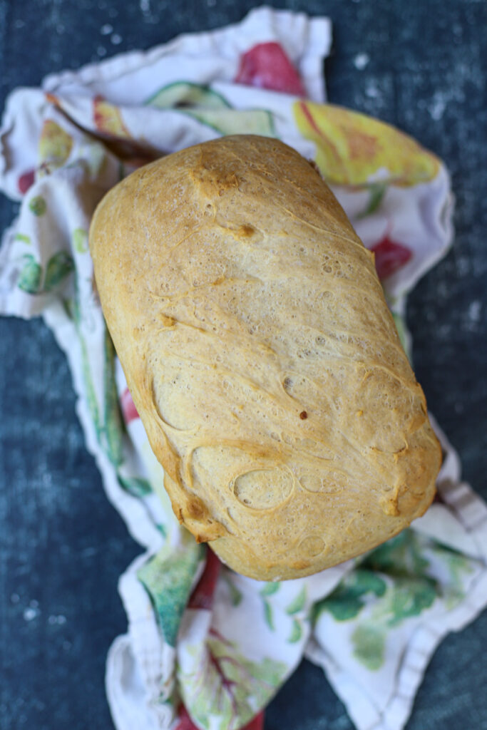 Golden brown loaf of cottage cheese bread resting on a colorful tea towel on a dark textured background.