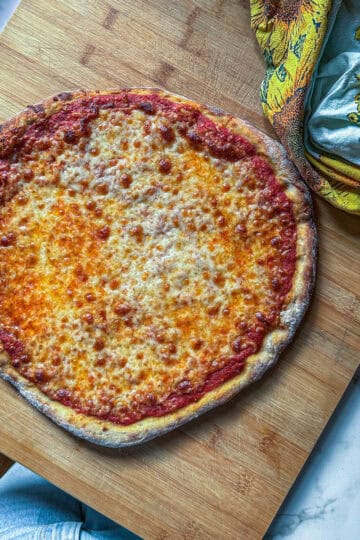 Golden, homemade cheese pizza topped with a rich tomato sauce, served on a wooden board alongside a sunflower-patterned towel.