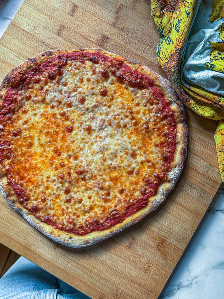 Golden, homemade cheese pizza topped with a rich tomato sauce, served on a wooden board alongside a sunflower-patterned towel.