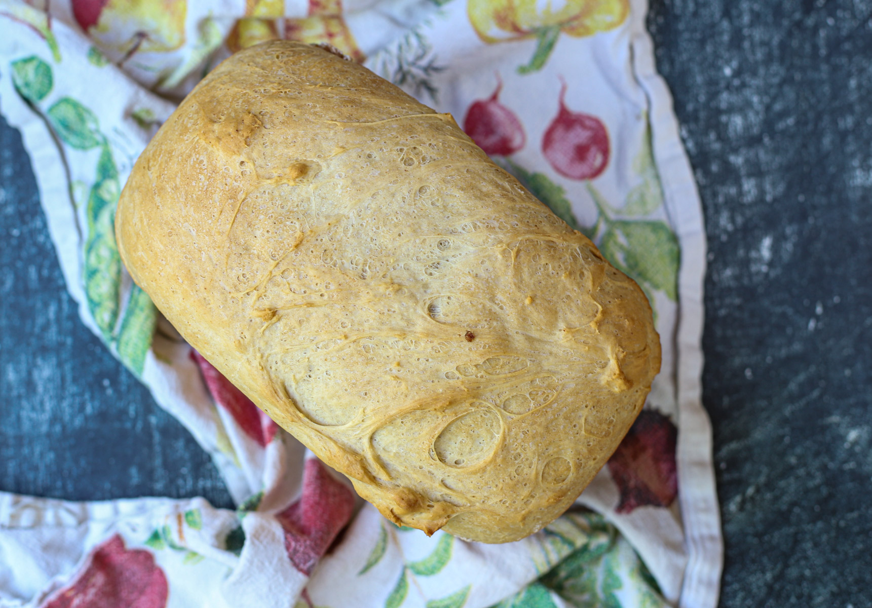 Rustic loaf of cottage cheese bread on a colorful tea towel, showcasing a soft crust and airy texture.