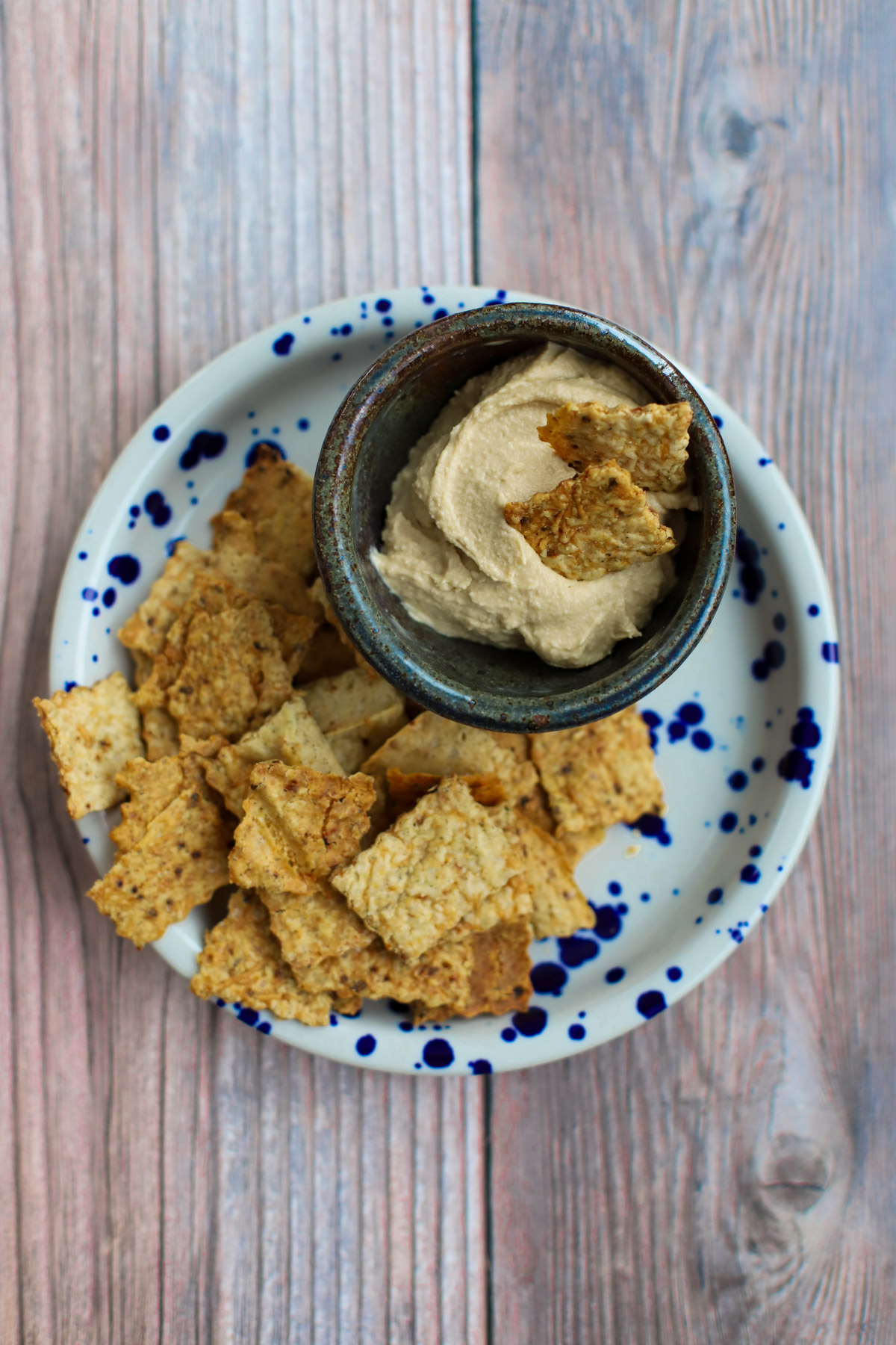 Crispy sourdough discard crackers on a blue and white speckled plate, paired with a bowl of creamy hummus topped with crackers.