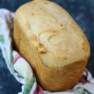 Tall, golden loaf of cottage cheese bread with a soft crust, resting on a patterned kitchen towel.