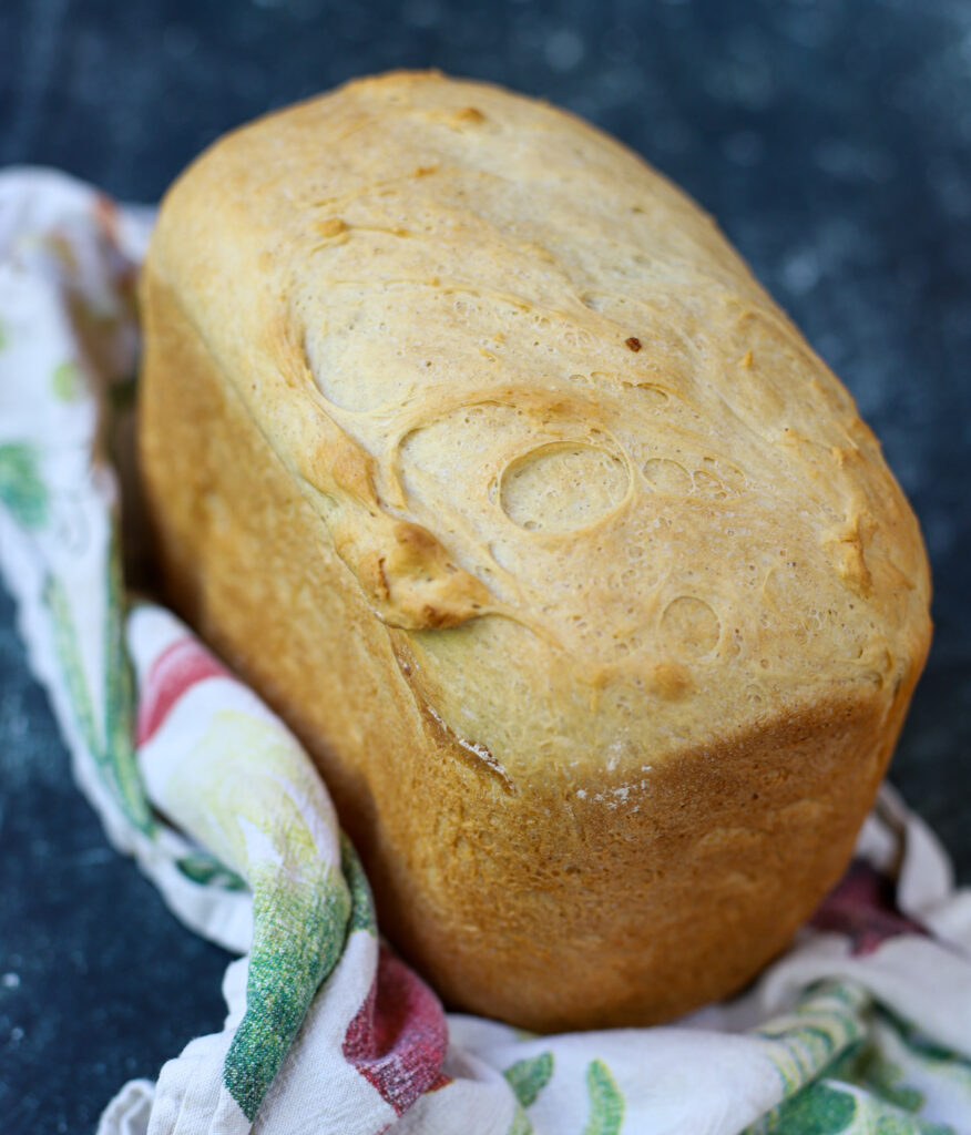 Tall, golden loaf of cottage cheese bread with a soft crust, resting on a patterned kitchen towel.