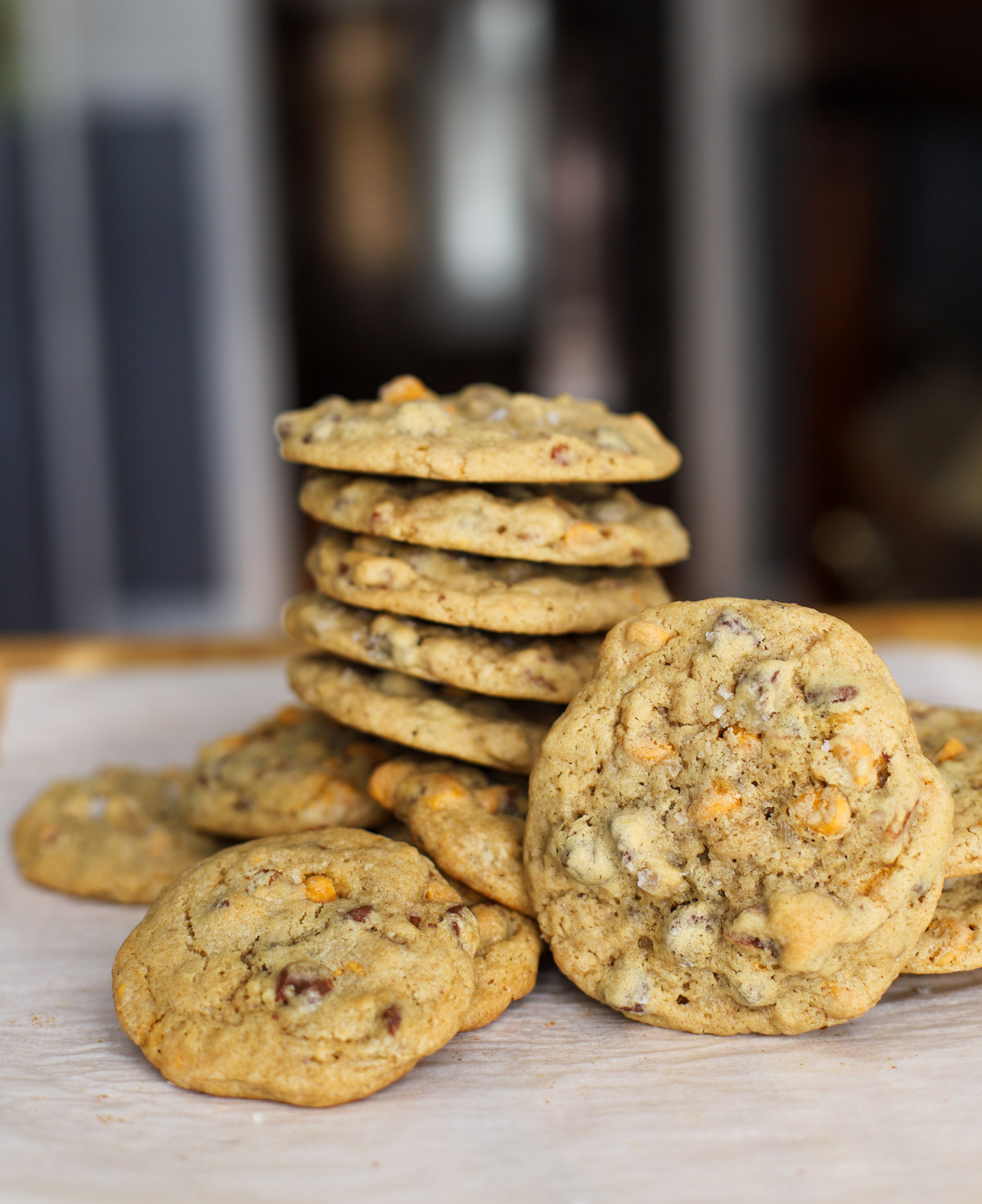 Close-up of sourdough chocolate chip cookies with butterscotch chips and toasted pecans, featuring a stack and individual cookies on parchment paper.