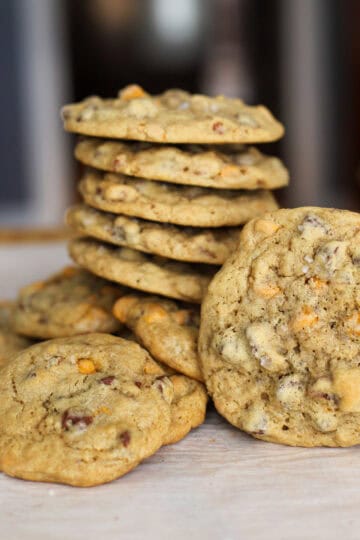 A stack of sourdough chocolate chip cookies with butterscotch chips and toasted pecans on parchment paper, showcasing their golden texture and mix-ins.