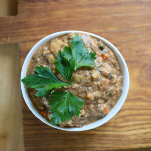 Close-up of a bowl of creamy vegan clam chowder topped with fresh parsley, placed on a rustic wooden surface.