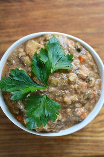 Close-up of a bowl of creamy vegan clam chowder topped with fresh parsley, placed on a rustic wooden surface.