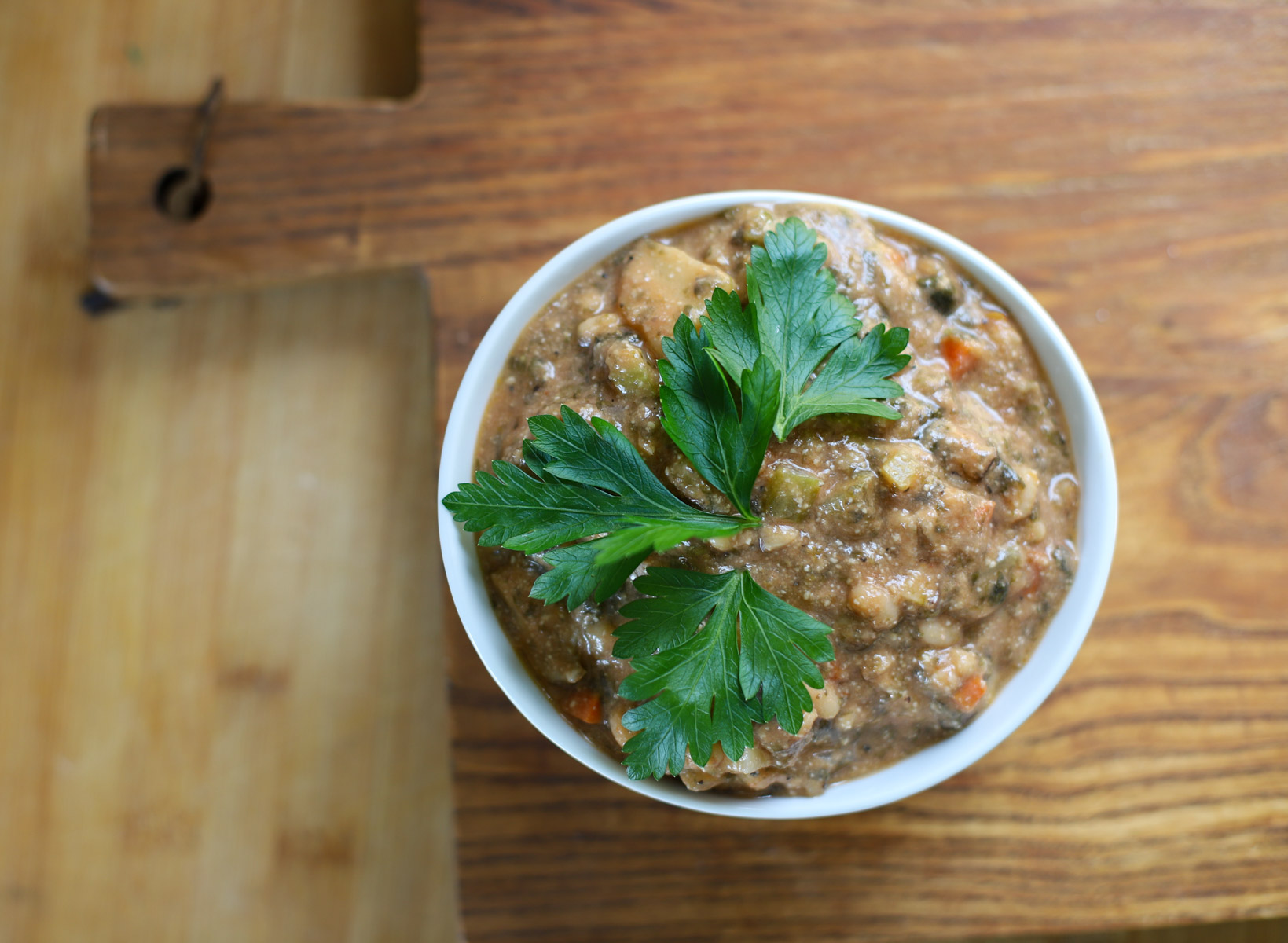 A white bowl filled with creamy vegan clam chowder, garnished with fresh parsley leaves, placed on a rustic wooden cutting board.