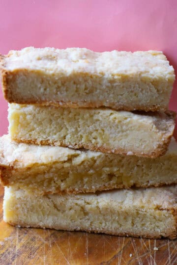A stack of homemade Ted Lasso biscuits with a crumbly shortbread texture, resting on a wooden surface against a pink background.