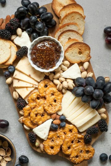 A gourmet charcuterie board featuring Trader Joe’s cheeses, crackers, pretzels, nuts, and fresh fruit, arranged with fig jam for the perfect snack spread.