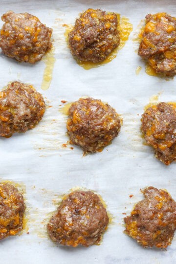 Freshly baked sausage patties with melted cheese and browned edges cooling on a parchment-lined tray.