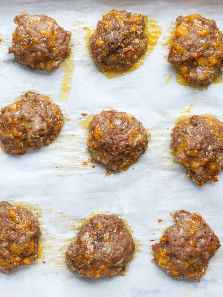 Freshly baked sausage patties with melted cheese and browned edges cooling on a parchment-lined tray.