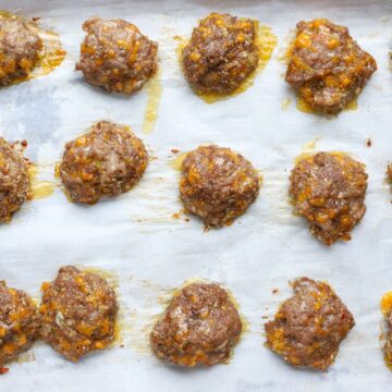 Crispy edges and melted cheddar on juicy baked sausage patties arranged on a parchment-lined baking sheet.