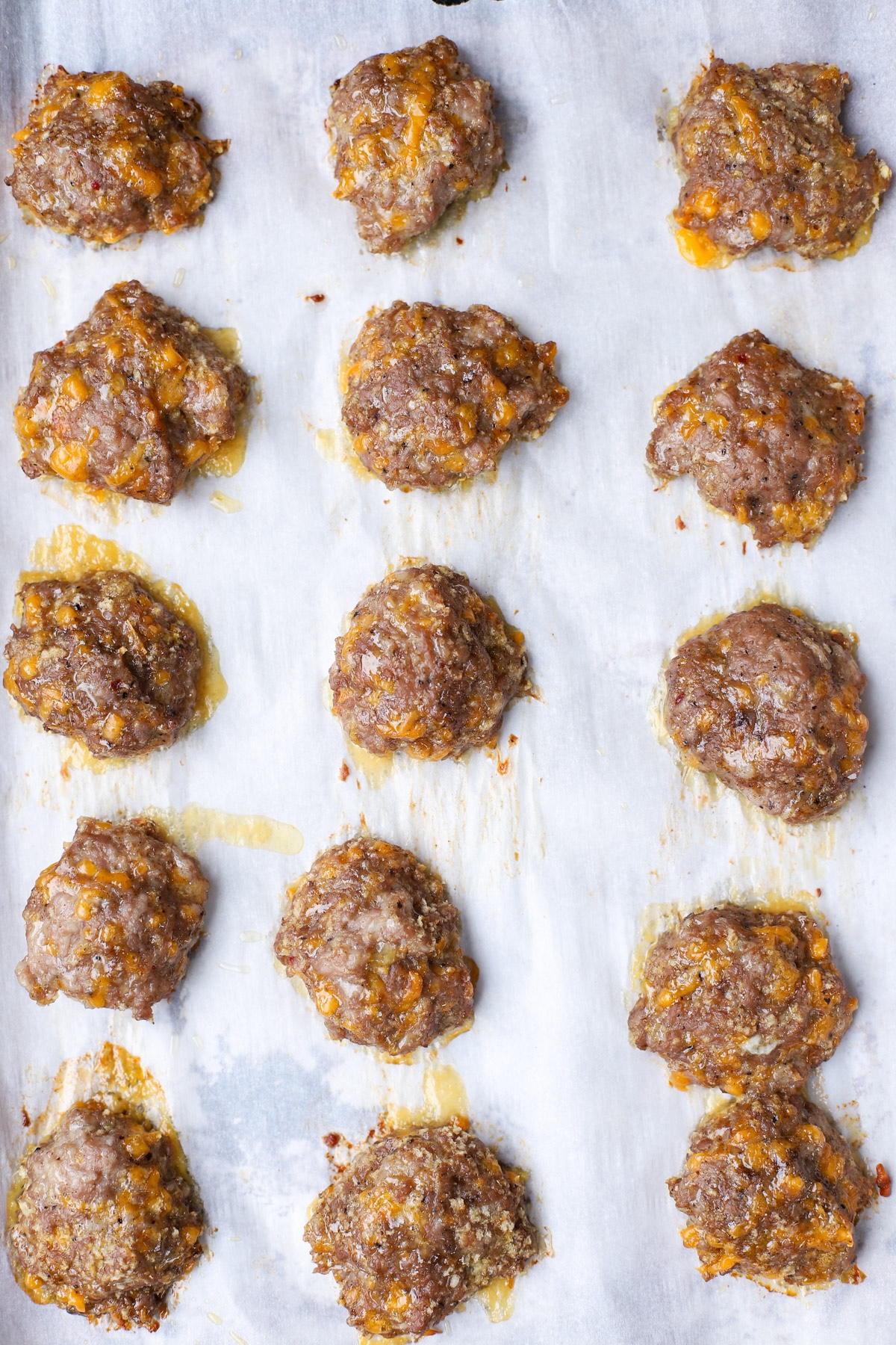 Golden brown baked sausage patties with melted cheddar on a parchment-lined baking sheet, fresh from the oven.