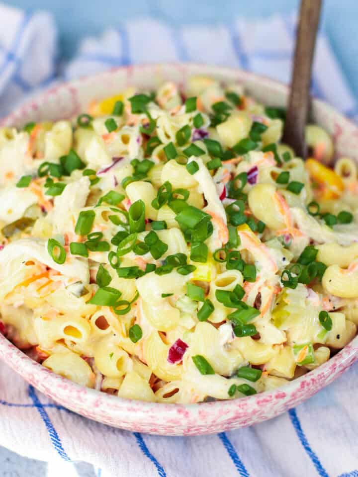 A vibrant bowl of creamy chicken macaroni pasta salad, featuring tender pasta, shredded chicken, crisp coleslaw mix, and a creamy dressing, generously garnished with fresh green chives, set on a blue and white checkered cloth.