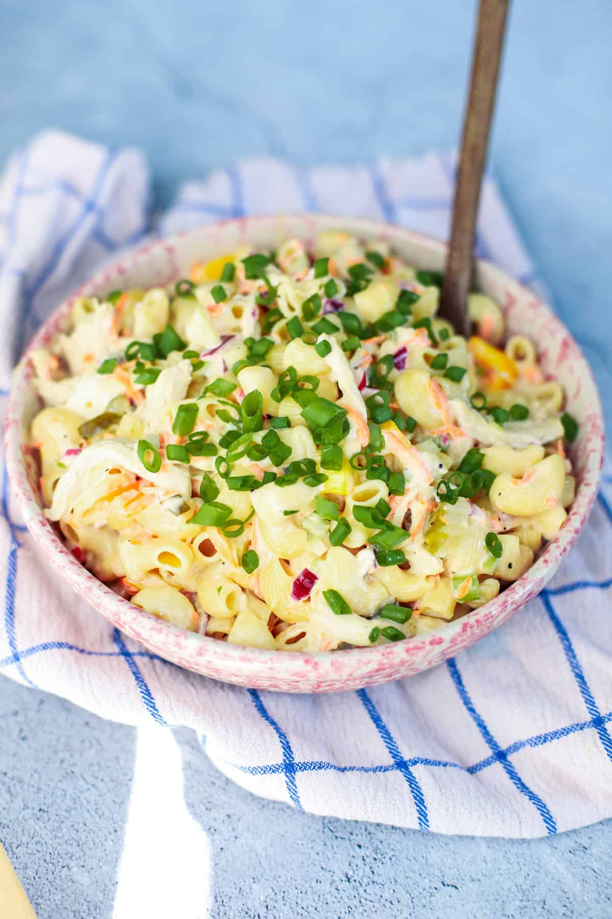 Close-up of a creamy chicken macaroni pasta salad topped with sliced green onions, served in a pink speckled bowl on a checkered dish towel.