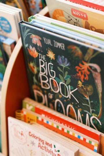 Close-up of a wooden book rack displaying children's nature and gardening books, including 'The Big Book of Blooms' and colorful activity books.