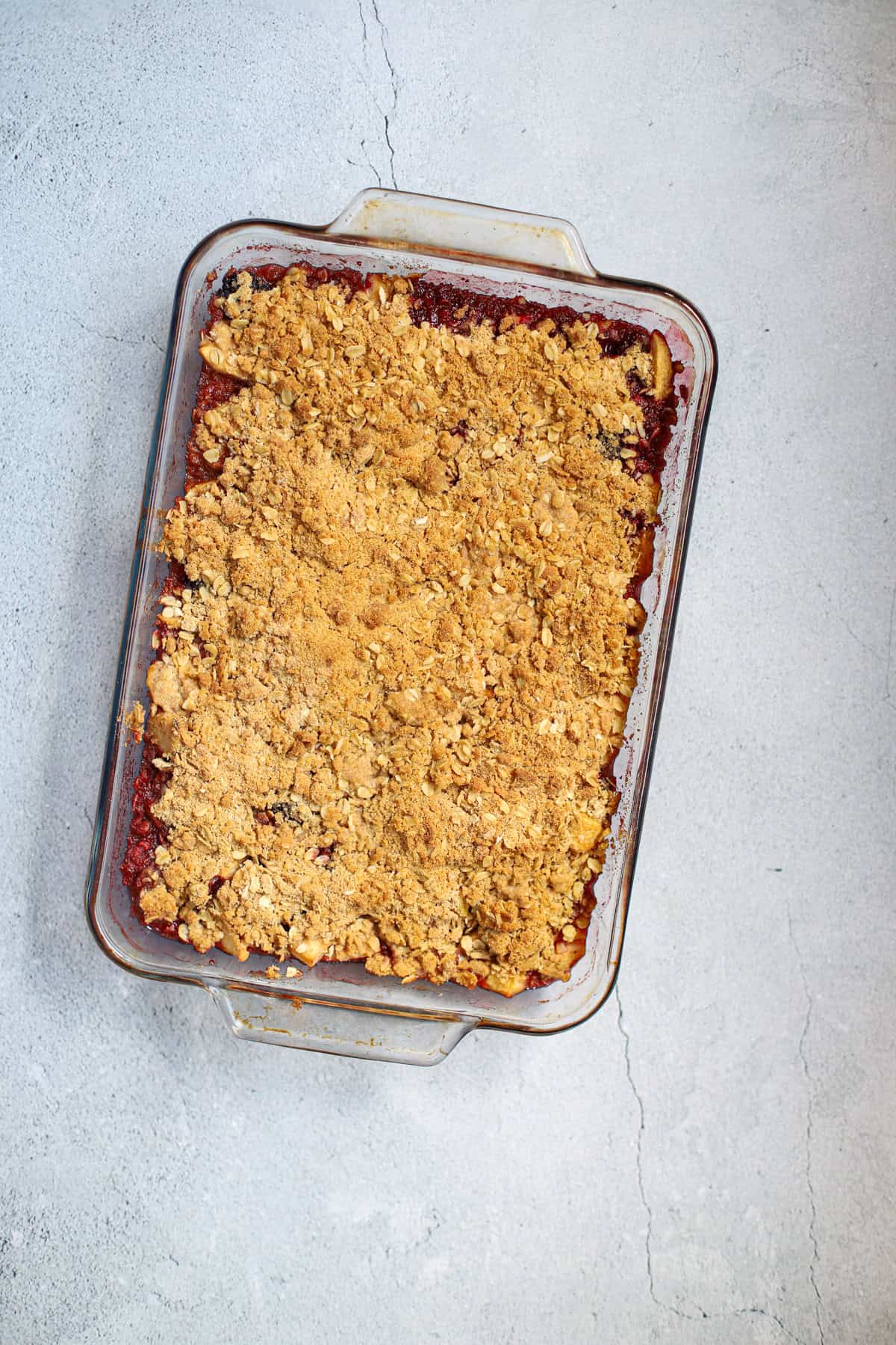 Homemade apple blackberry crumble baked in a glass dish with golden brown oat topping.