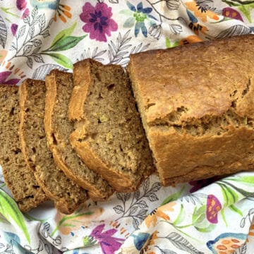 A freshly baked and sliced loaf of rich, moist yellow squash bread sitting on a colorful floral tea towel, showcasing the beautiful crumb texture of the quick bread.