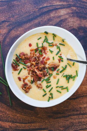 Overhead view of easy loaded potato soup in a white bowl topped with crispy bacon and fresh chives