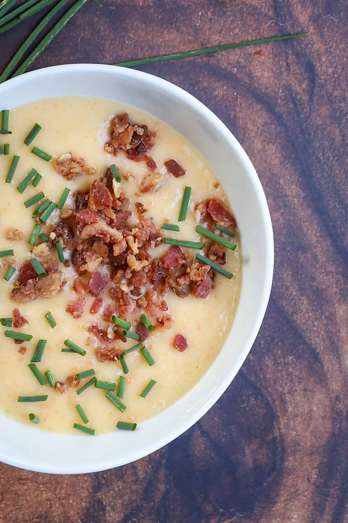 Close-up of loaded potato soup showing crispy bacon crumbles and snipped chives on a smooth, creamy surface