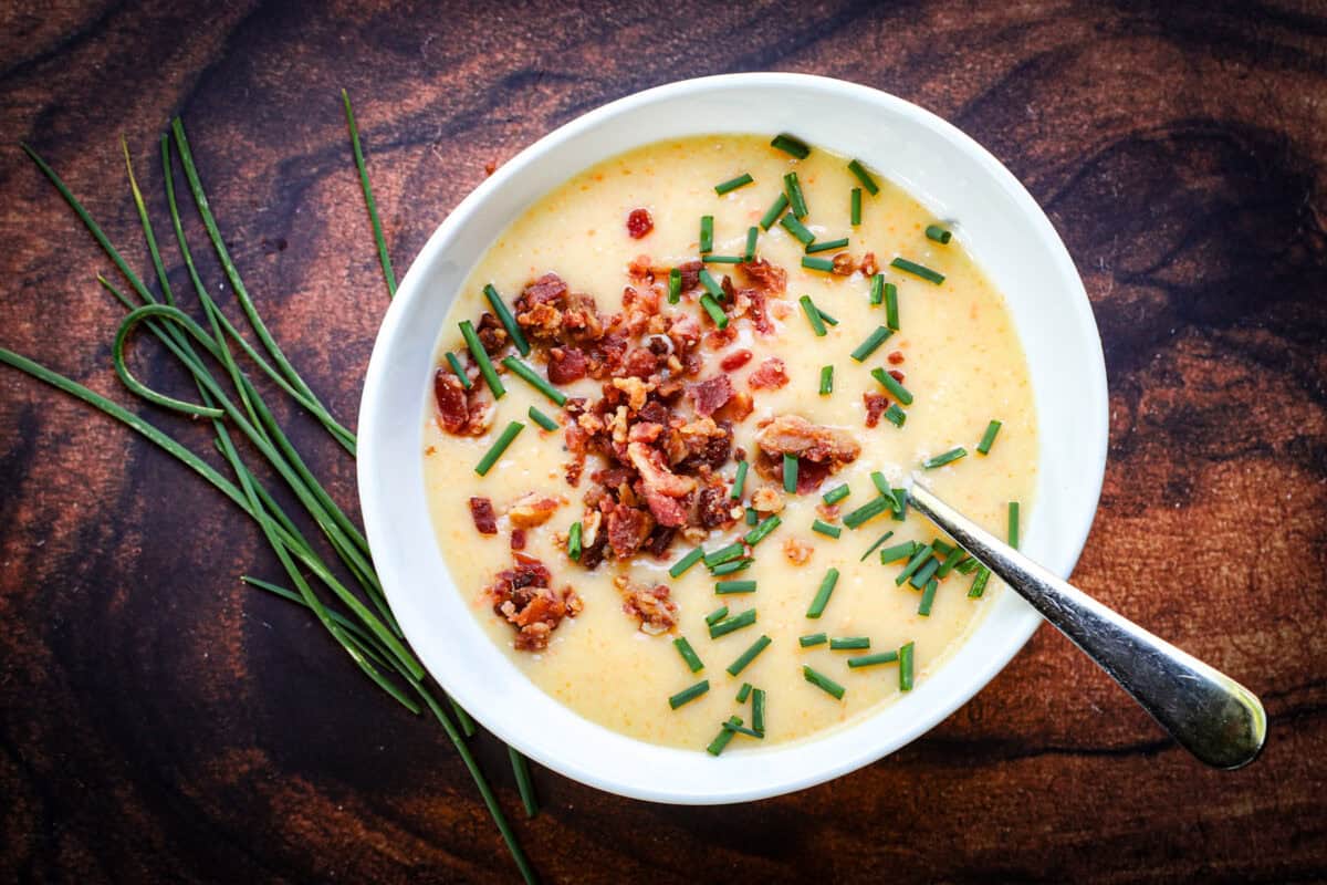 Bowl of loaded potato soup with bacon and chives beside a bundle of fresh chives on a rustic wood surface