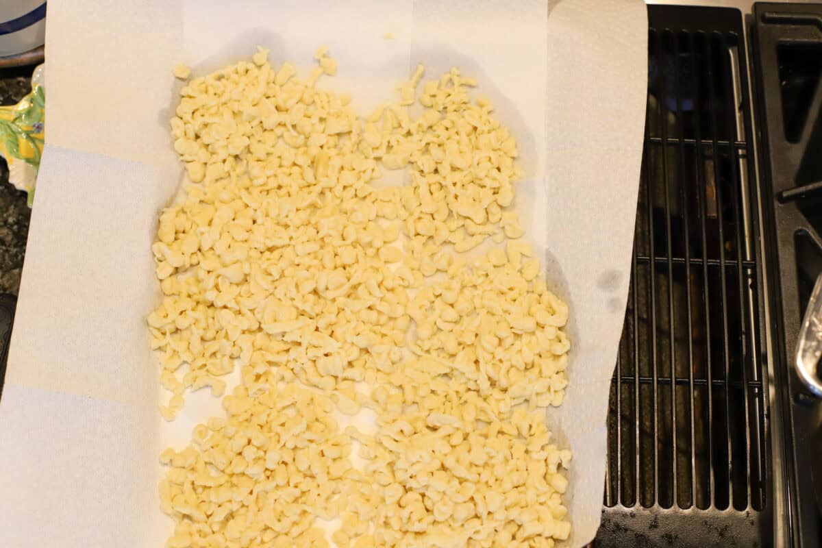 Freshly cooked spaetzle spread out on paper towels to drain next to the stove