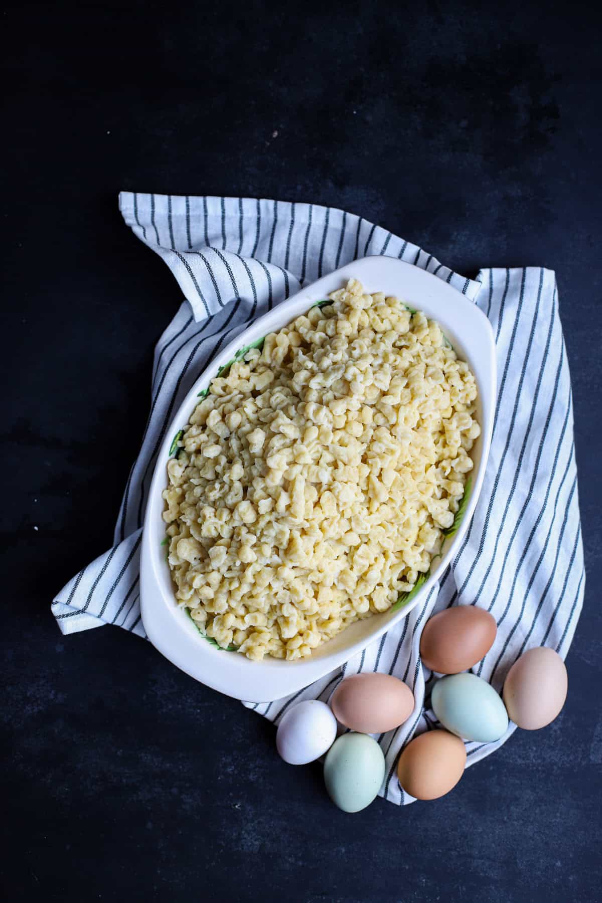 Dish of freshly cooked spaetzle with brown, blue, and white eggs on a blue-striped kitchen towel