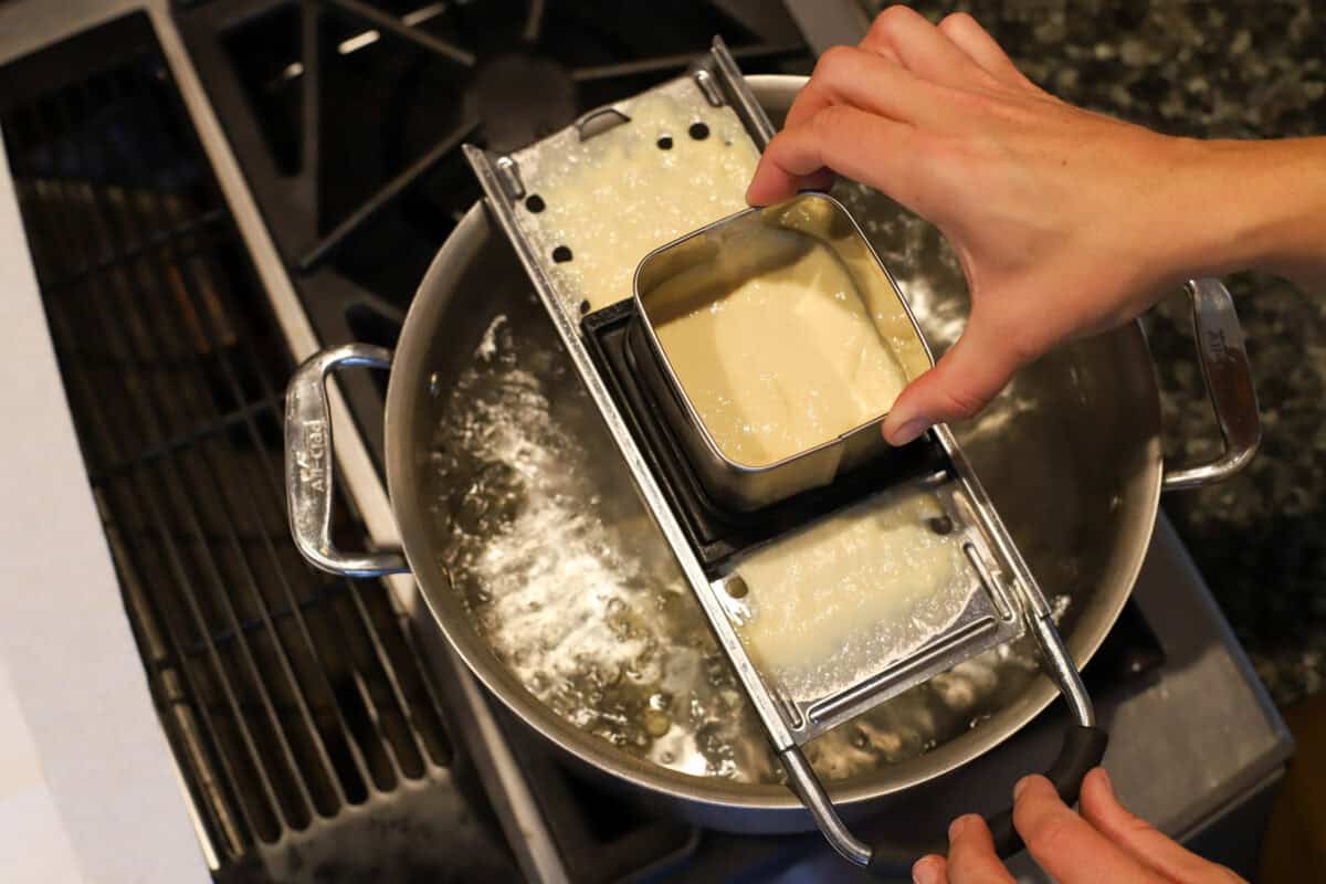 Hand sliding a spaetzle maker filled with batter back and forth over a pot of boiling water