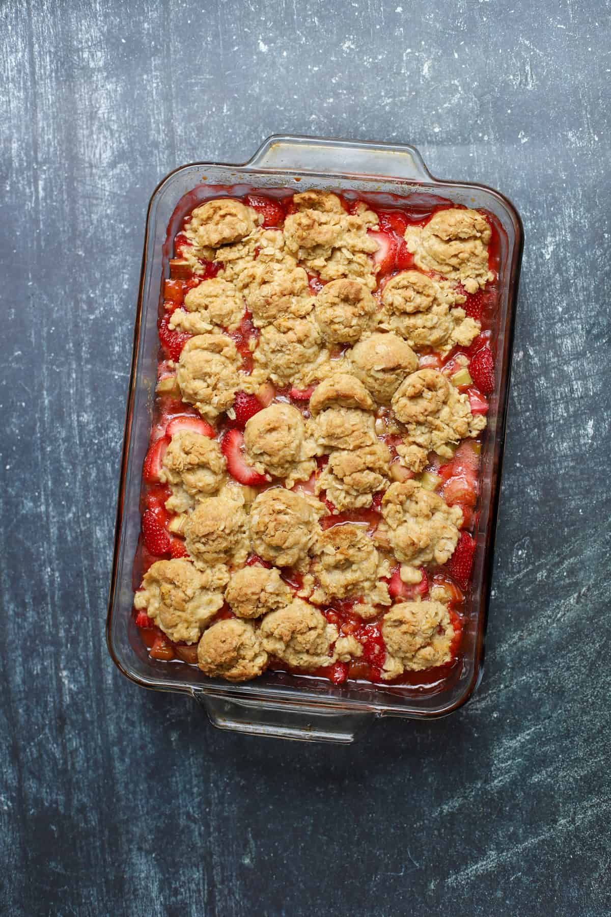 Overhead view of strawberry rhubarb crumble with golden oat topping in a rectangular glass baking dish